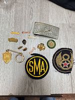 Group overview of belt buckle, keychain, eight pins, two patches