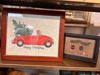 Both framed folk art pieces side by side on shelf