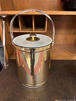 Full view of cylindrical mirrored gold ice bucket with lucite handle and lid