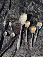 All seven spoons laid out on dark fabric, showing relative sizes and tarnish