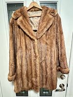 Front view of honey-tan mink jacket hanging, showing shawl collar, rolled cuffs, toggle closure