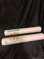 Two sealed rolls vinyl wallpaper on black fabric backdrop