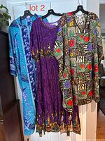 Three caftans hanging: blue floral, purple print, multicolour geometric print