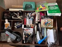 Plastic compartment tray filled with staplers, staple removers, labels, tabs, glue, push pins and other small supplies