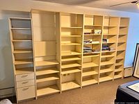 Front view of entire modular wall bookcase system showing six tall shelving units, drawer unit on left, open shelves, off-white finish