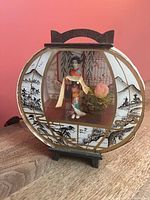 Front view of illuminated lamp showing geisha figure and scenic panels