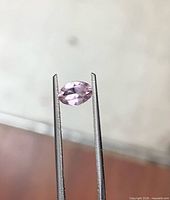 Gemstone held by tweezers showing oval profile and color