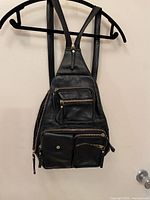 Full view of black leather sling backpack hanging, showing overall design and pockets