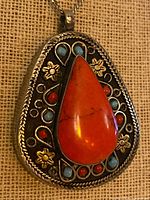 Front view of pendant showing coral centre stone, turquoise and red accents, sterling silver setting