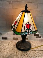Full view of lamp illuminated showing stained glass shade and metal base
