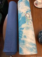 Two rolled yoga mats on table—blue-white Alo mat and dark blue mat
