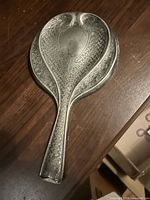 Back view of ornate silver-tone metal hand mirror showing raised pattern and handle