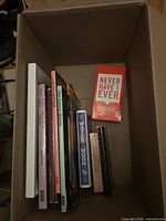 Box containing Never Have I Ever game, Water Moon disc, several books and media cases