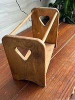 Angled view of wooden magazine rack showing one side panel with heart cutout, both dowel rails and base