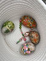 Four hand-painted eggs and pastel bead strand inside white woven basket