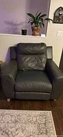 Front view of dark leather recliner armchair showing padded seat, back, armrests and wooden feet