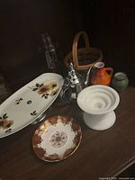 Group shot of platter, saucer, metal teapot, milk glass compote, ceramic pitcher, vase, glass bottle, basket