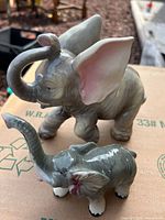 Large and small glazed gray ceramic elephant figurines on cardboard surface