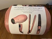 Front of pink pouch with product sleeve showing images of dryer, flat iron and wand