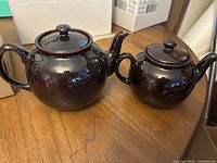 Large and small brown glazed teapots side by side on table