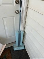 Full view of teal stick vacuum leaning against door