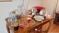 Overall lot on wooden table showing glass jars, vases, bowls, decorative plates, ceramic pieces