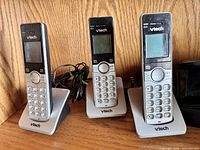 Three VTech silver cordless handsets standing on individual charging cradles with power cords visible