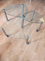 Three triangular glass tables nested together, view from side