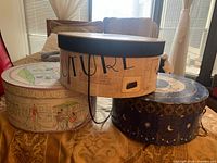 Three of four printed round hat boxes showing newspaper, café, and blue star designs