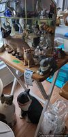 Overall lot on folding tray table showing multiple figurines, display cabinet and large cat figure on floor