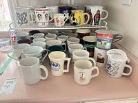 Overview of mugs on countertop and rack showing quantity and variety of prints