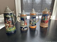 Front view of all four German steins showing decorative scenes and lids