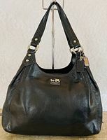 Front view showing black leather, logo plaque, handles, hangtag