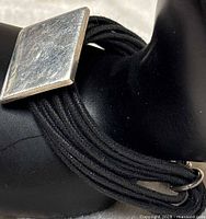 Bracelet close-up showing square sterling silver plaque and multiple black leather strands