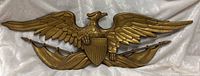 Full view of gold tone eagle wall plaque on fabric backdrop
