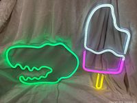 Both neon signs lit: green dinosaur head and multicolour popsicle