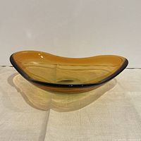 Side profile of amber freeform glass bowl showing undulating rim and low profile