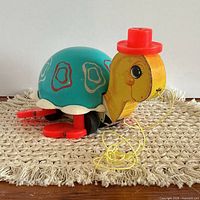 Left side view showing wooden head, red hat, shell pattern, feet, pull string