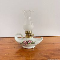 Front view showing porcelain base, floral motif, brass burner, and glass chimney