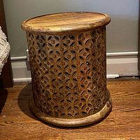 Full view of carved drum side table placed on floor