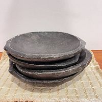 Stacked view of four charcoal stone bowls showing exterior texture and irregular rims