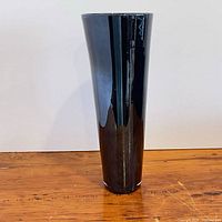 Full frontal view of tall black glass vase on wooden surface