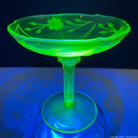 Compote glowing green under UV showing floral etch and pedestal