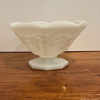 Side view of white milk glass pedestal bowl showing grape relief and hexagonal foot