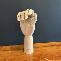 Front view of closed-fist articulated wood hand on base