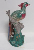 Right side view of multicolour ceramic peacock figurine on tree stump