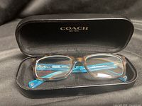 Eyeglasses in open Coach hard case showing frame front and case branding