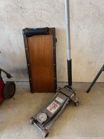 Floor jack front view beside wood mechanic creeper