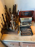 Large twist drill bits in block, two open metal boxes with contents