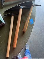 Three hand garden pick hoes on tabletop showing heads and handles